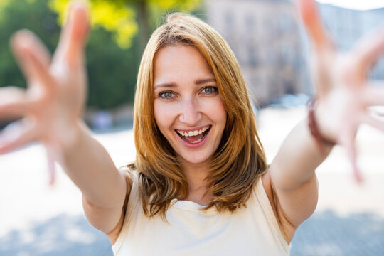 Smiling woman reaches toward the camera outdoors in Berlin