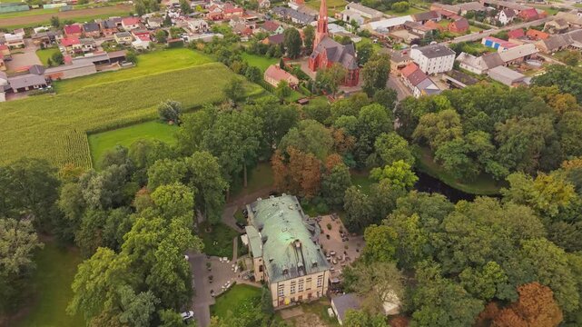 Aerial view of Palace in Pakoslaw surrounded by lush trees, a small pond, and nearby village buildings in Pakoslaw, Wielkopolskie, Poland.