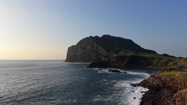 Aerial view of the volcanic tuff cone Seongsan Ilchulbong rising above the ocean waves along the coastline in Seogwipo-si, Jeju-do, South Korea.