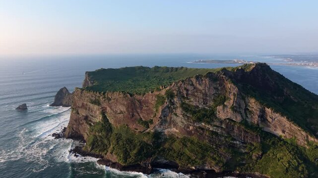Aerial view of Seongsan Ilchulbong, a volcanic tuff cone rising from the sea with lush green crater and steep rocky cliffs in Seogwipo-si, Jeju-do, South Korea.