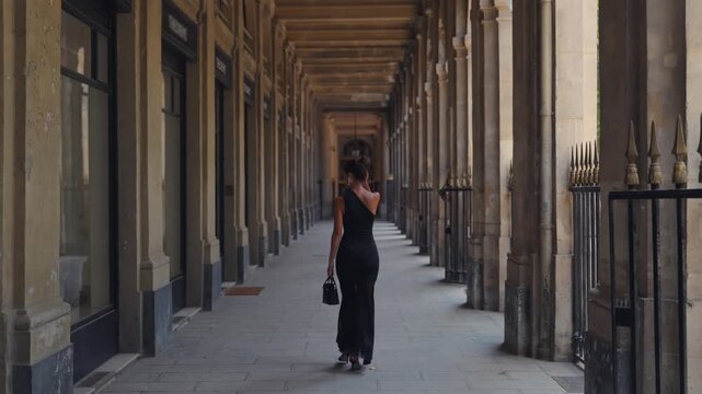 Woman in black dress walking through historic Paris colonnade
