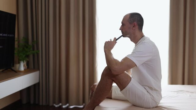 Man sitting on bed in front of TV, choosing what to watch using remote control.