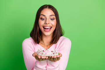 Young woman in pink sweater holding a tiara smiles brightly against a green background for fashion lifestyle stock photo © deagreez