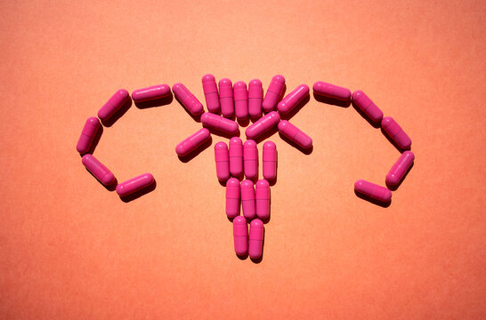 Pink capsules arranged in the shape of a uterus on a textured orange background, symbolizing women's health and reproductive wellness in a creative visual representation