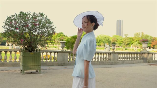 Woman in white hat walking past flowering tree in Luxembourg Gardens