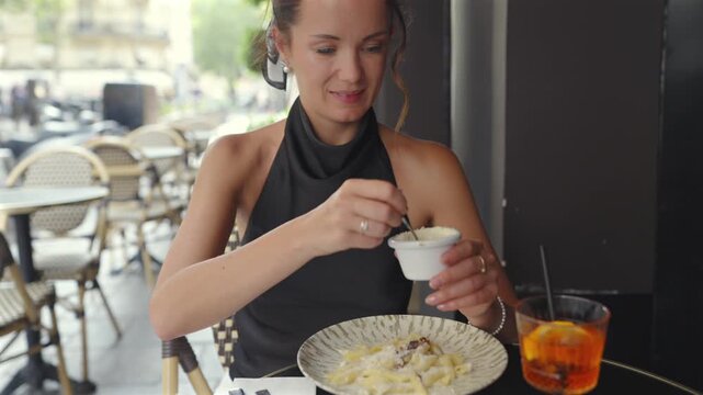 Woman sprinkling cheese on pasta at Paris sidewalk cafe
