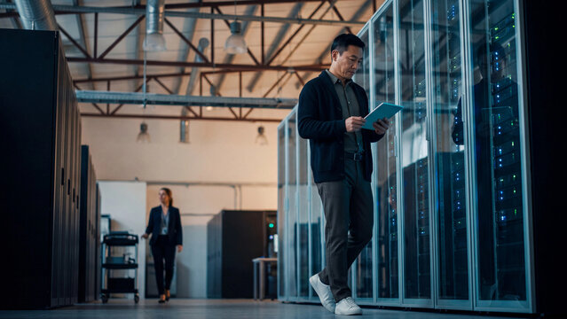 A data center employee checks data on a tablet at a rack in the server room.