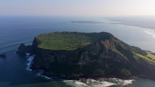 Aerial view of the lush green crater of Seongsan Ilchulbong volcanic tuff cone surrounded by steep cliffs and the ocean in Seogwipo, Jeju-do, South Korea.