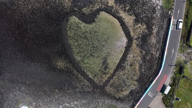 Aerial view of the heart-shaped stone fish trap at Udo island with dark volcanic rocks and clear shallow water along the coastal road in Cheju, Jeju-do, South Korea.
