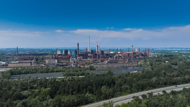 Aerial view of the Dolni Vitkovice steelworks and heavy industrial complex with tall chimneys and metal structures surrounded by forests and a highway in Ostrava, Moravian-Silesian Reg, Czechia.
