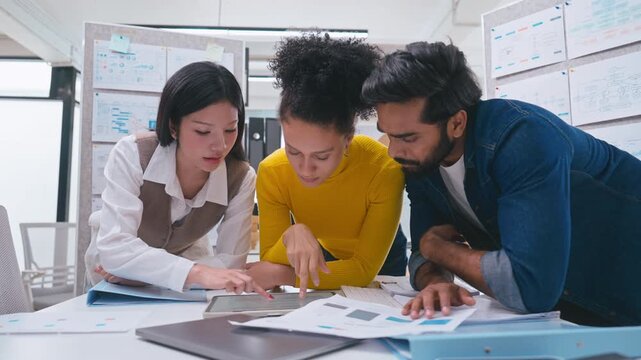 Corporate professionals gathering around a digital tablet, looking seriously at the screen to solve a problem and discuss business strategy.