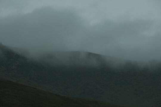 A dark, moody mountain landscape covered in thick fog and low clouds. This minimalist, atmospheric image 