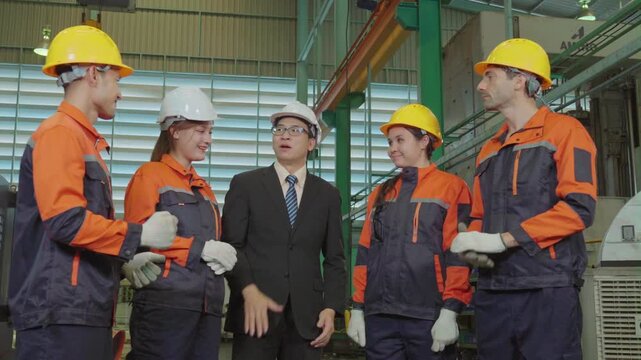 A diverse factory team and manager stack hands together celebrating success, smiling with joined hands and high five gesture inside an industrial manufacturing plant.