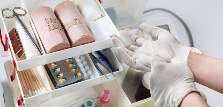 Medical professional preparing first aid supplies with sterile gauze, bandages, medical instruments and gloves on a stainless steel tray for wound care.