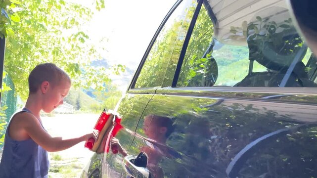 horizontal video of boy carefully helping to wash the car with interest. concept of involving children in family chores, fostering helpfulness, and encouraging quality family time spent productively