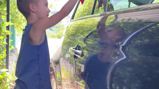 horizontal video of boy carefully helping to wash the car window. concept of involving children in family chores, fostering helpfulness, and encouraging quality family time spent productively