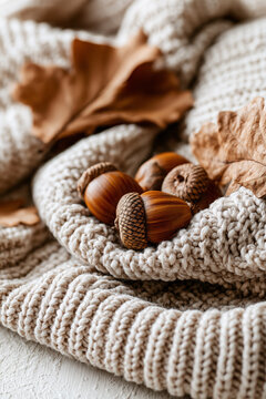 Cozy beige knitted wool blanket paired with scattered natural acorns and dry autumn leaves.