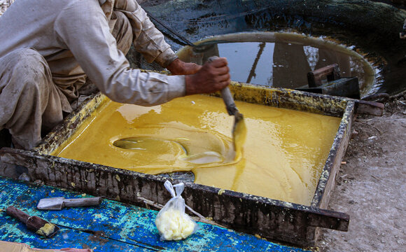 View of a worker stirring liquid jaggery in a wooden tray during the traditional production process in Multan, Punjab, Pakistan.