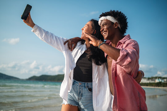 Diverse couple connected, embracing technology and social media while enjoying moments at the beach