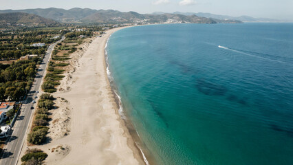 Obraz premium Panoramic view of long sandy beach next to turquoise sea and coastal road.