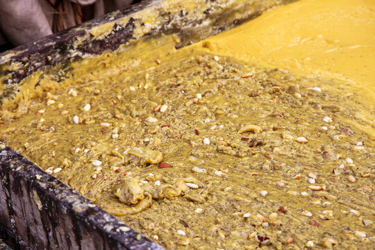 View of traditional jaggery being prepared in a large wooden container, mixed with nuts and seeds in Multan, Punjab, Pakistan.