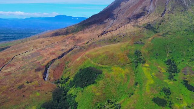 Aerial view of the volcanic slopes of Mount Sinabung with lush green vegetation and rugged terrain in Naman Teran, North Sumatra, Indonesia.
