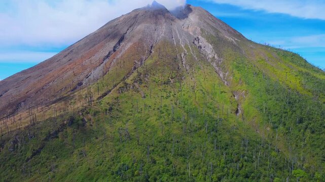Aerial view of Mount Sinabung volcano with steam rising from the crater and lush green slopes in Naman Teran, North Sumatra, Indonesia.