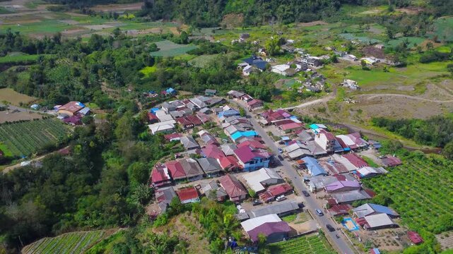 Aerial view of Mount Sinabung and village with red-roofed houses surrounded by lush agricultural fields and green hills in Naman Teran, North Sumatra, Indonesia.