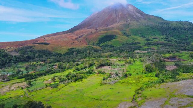 Aerial view of Mount Sinabung with lush green fields and volcanic slopes in Naman Teran, North Sumatra, Indonesia.