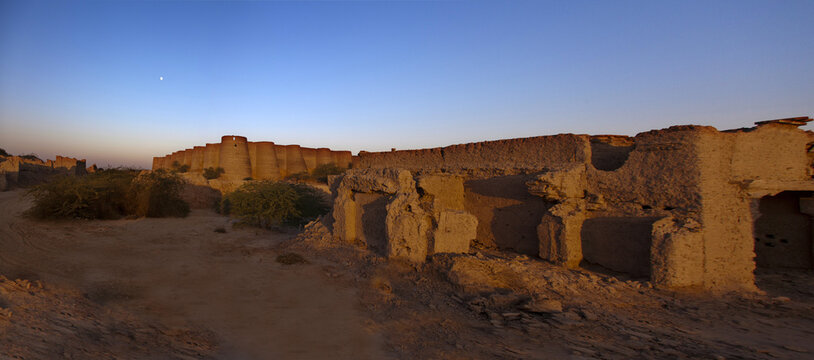 View of the massive mud-brick walls of the historic Derawar Fort under the golden hour light in the desert landscape of Derawar, Punjab, Pakistan.