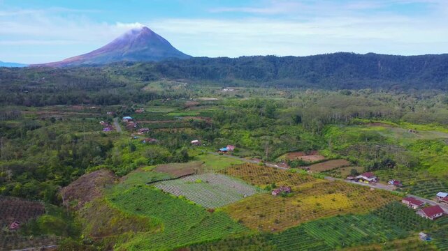 Aerial view of Mount Sinabung rising above lush agricultural fields and rural landscape in Naman Teran, North Sumatra, Indonesia.