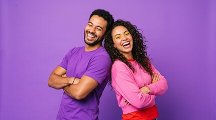 Obraz premium Happy couple enjoying a lighthearted moment together back-to-back with crossed arms against purple wall.