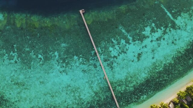 Aerial view of a long wooden pier extending into the turquoise waters of Raja Ampat Regency, Kri Island, Southwest Papua, Indonesia.
