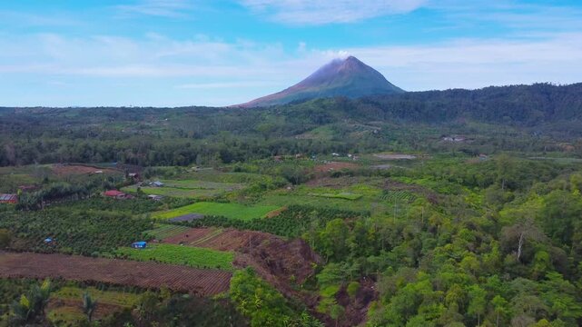 Aerial view of Mount Sinabung volcano rising above the lush agricultural fields and dense forests of Naman Teran, North Sumatra, Indonesia.