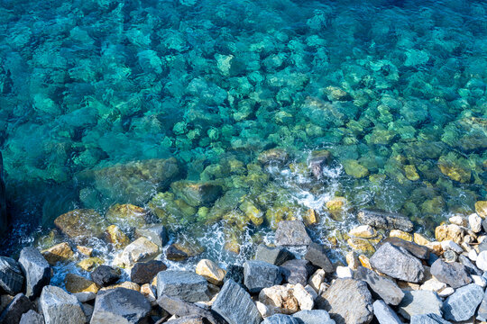 Aerial view of clear turquoise water crashing against rocky cliffs along the coast of Italy.