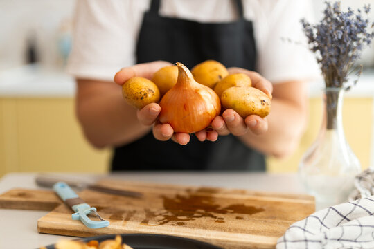 Hands holding an onion and small potatoes over a wooden cutting board for kitchen cooking preparation and home meal background