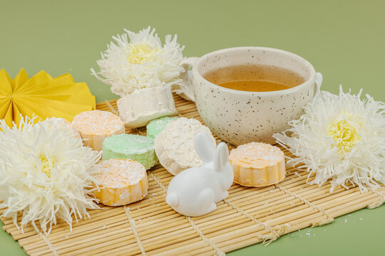 Mid-Autumn Festival flat lay with mooncakes, green tea cup, white rabbits, chrysanthemums, paper fan