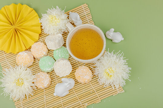 Mid-Autumn Festival flat lay with mooncakes, green tea cup, white rabbits, chrysanthemums, paper fan