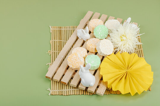 Traditional mooncakes on a wooden stand with ceramic rabbits, paper fan, chrysanthemum, bamboo mat
