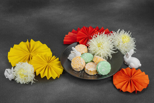 Traditional Chinese mooncakes on a plate with paper fans, ceramic rabbits, and chrysanthemums