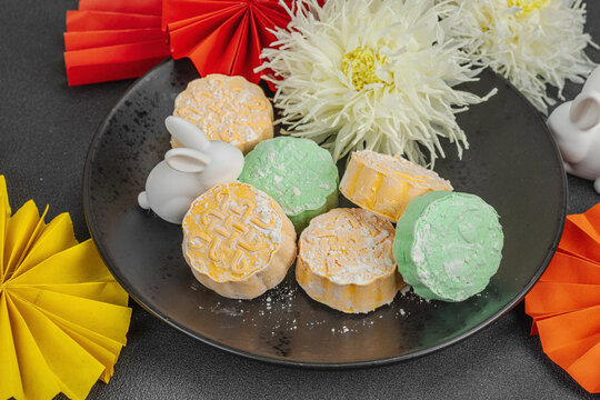 Traditional Chinese mooncakes on a plate with paper fans, ceramic rabbits, and chrysanthemums