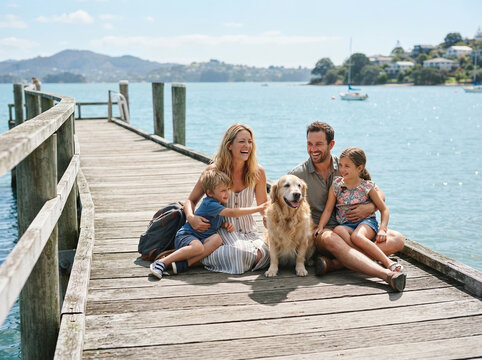 Family of four and a golden retriever seated on a wooden lakeside pier