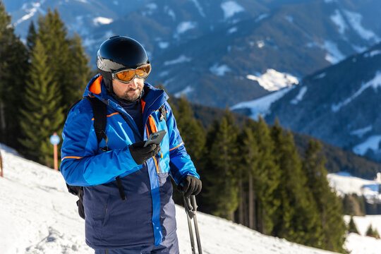 Young adult skier use smartphone make selfie navigate online map app winter alpine skiing resort. Male sporty person with backpack using mobile phone mountain Alps snow slope outdoors cold snowy day
