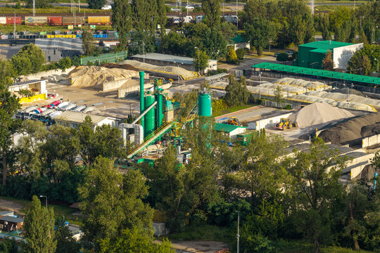 Aerial view of a large asphalt production facility featuring industrial silos, piles of raw aggregate materials, and parked concrete mixer trucks in an industrial area in Poland.