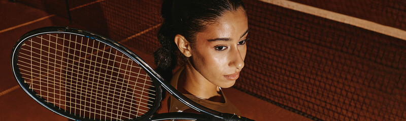 Young adult multiethnic woman holding tennis racket on court, focused during training match. Visual...