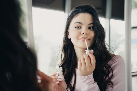 Young woman applying lip gloss in front of a mirror during a quiet beauty and self-care routine