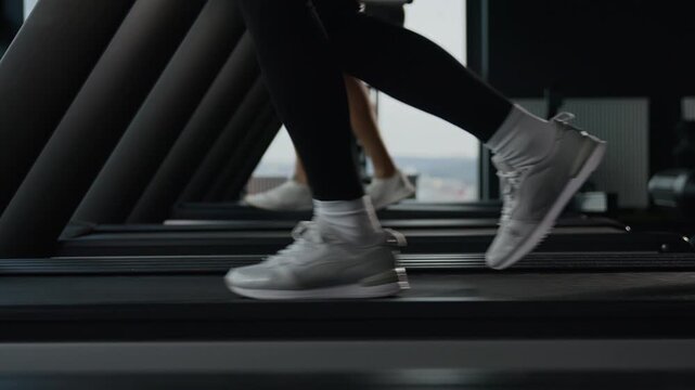 Close up multiethnic female and male legs running on treadmill in fitness gym sports shoes couple jogging cardio workout two runners moving run side view athletic family healthy people exercise indoor