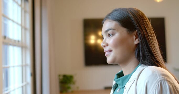 Woman wearing green top gazing at grid window, noticing movement, turning and smiling in lounge