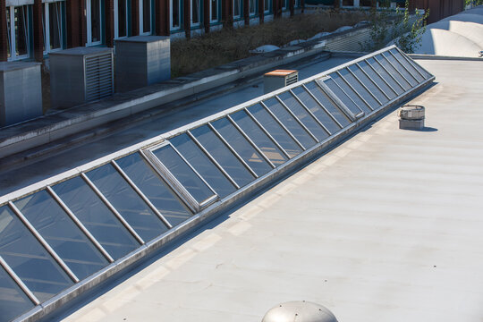 Architectural view of a modern building rooftop featuring a long glass skylight and vents.