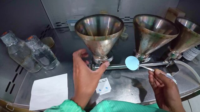 Scientist using tweezers to hold blue laboratory filter paper in facility